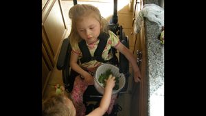 Two students, one holding the inner bowl of a salad spinner in their lap while the other student reaches in to grab green beans from inside